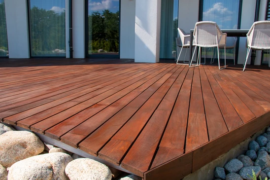 Terrasse extérieure en bois exotique avec lames décking alignées, mobilier design moderne incluant chaises tressées beiges et table