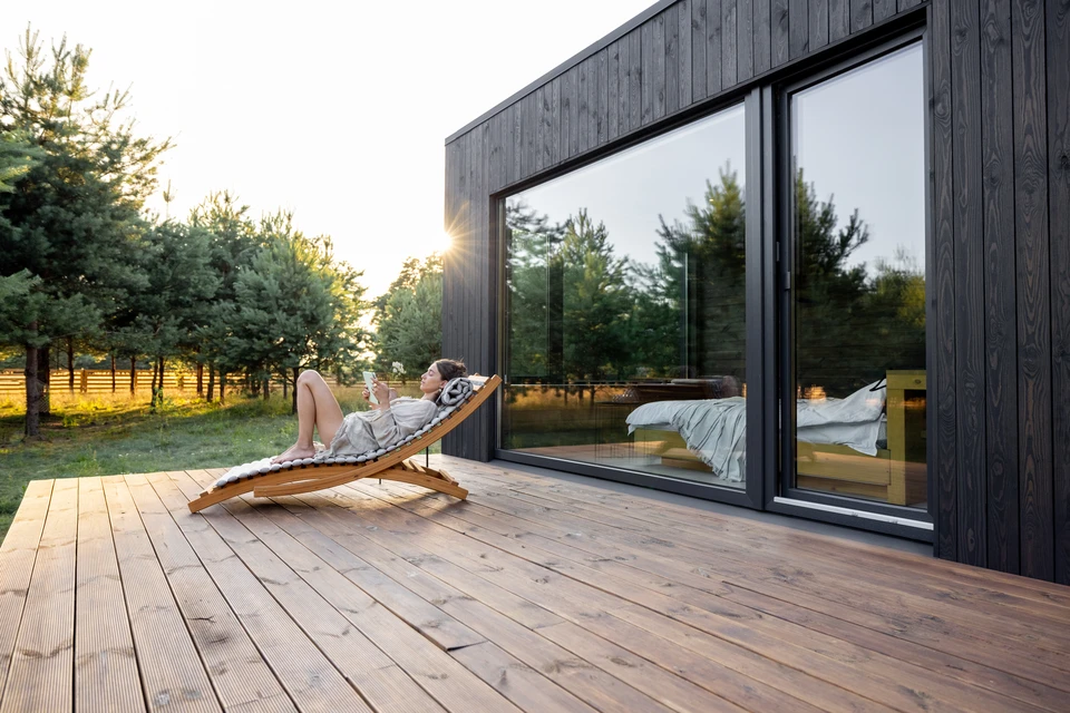Un ouvrier qualifié en tenue professionnelle installant une terrasse bois composite sur un chantier résidentiel en extérieur, avec des éléments de fabrication (structure préassemblée, outillage professionnel) visibles à proximité, illustrant la transition entre fabrication et pose sur le terrain. Lumière naturelle, contexte résidentiel réaliste.