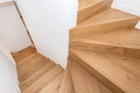 Escalier extérieur en bois massif avec plusieurs marches, installé dans un jardin ou donnant accès à une terrasse, montrant clairement la structure en bois naturel avec finition soignée, photographié en lumière naturelle de jour, entouré de végétation ou d'aménagements paysagers, représentant une création d'aménagement extérieur sur mesure.