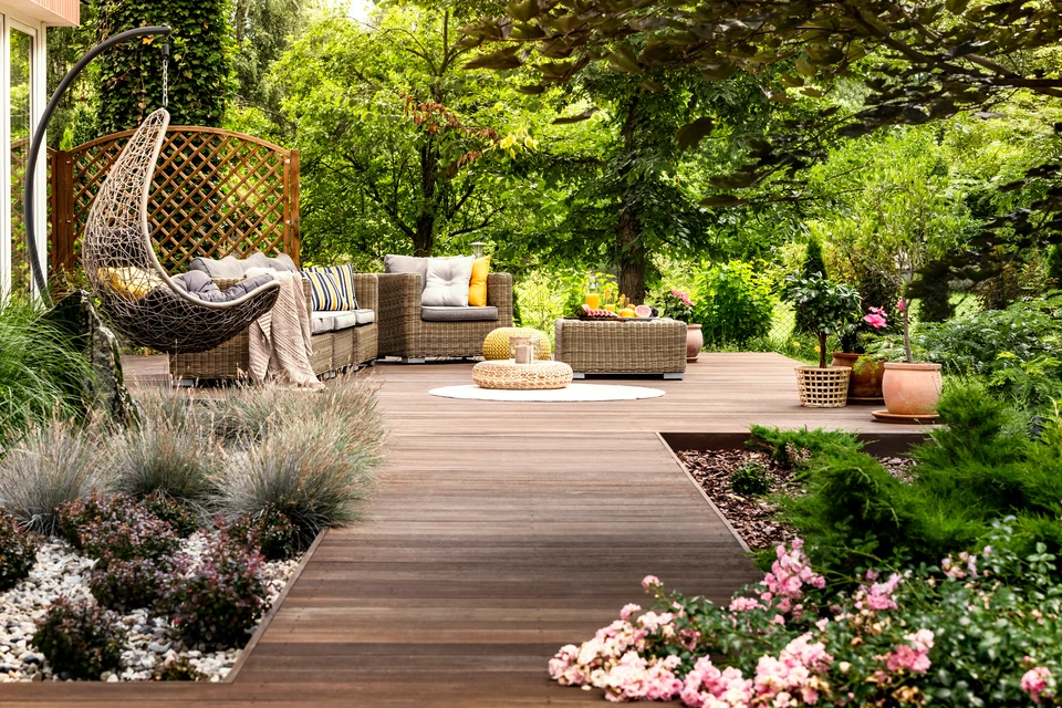 Terrasse extérieure aménagée avec salon de jardin en bois teck comprenant canapé deux places, deux fauteuils assortis avec coussins beiges, table basse carrée massive