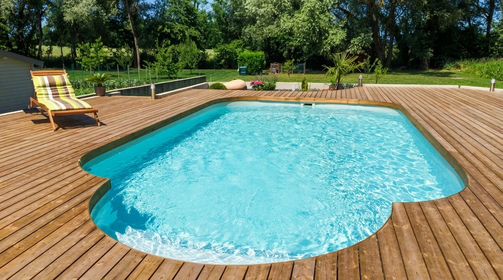 Terrasse en bois composite IPE entourant une piscine coque polyester ovale aux eaux turquoise