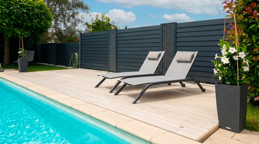 Piscine extérieure à débordement partiel avec terrasse en bois composite, entourée de végétation dense
