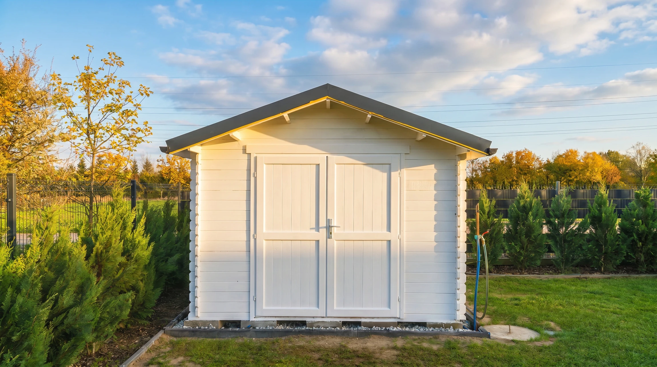 Jardin résidentiel avec abri de jardin en bois naturel à toit bombé, couverture bitumée grise, double porte battante avec ferrures noires