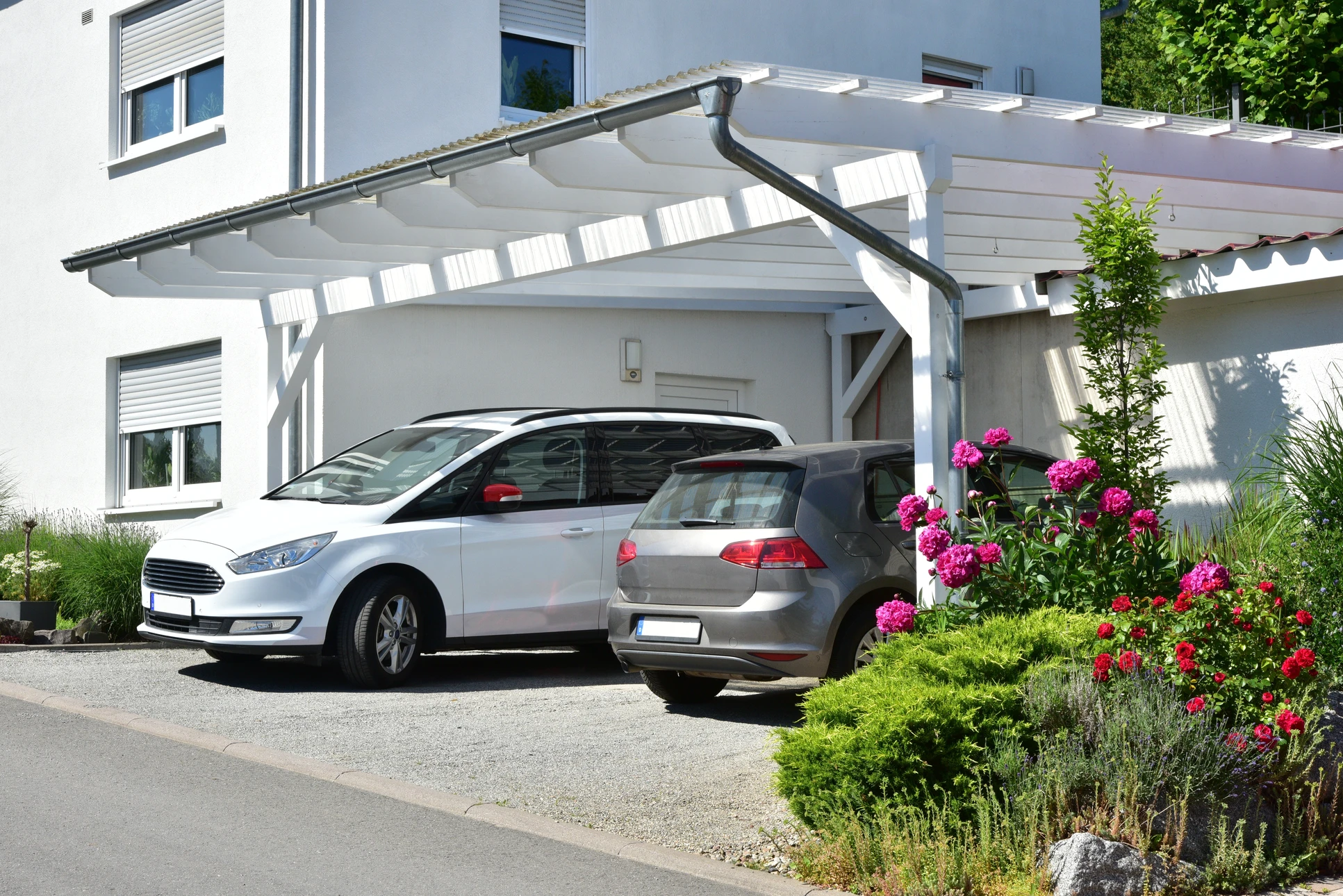 Carport moderne en bois avec structure à poteaux inclinés et toiture en ardoises, abritant une voiture noire