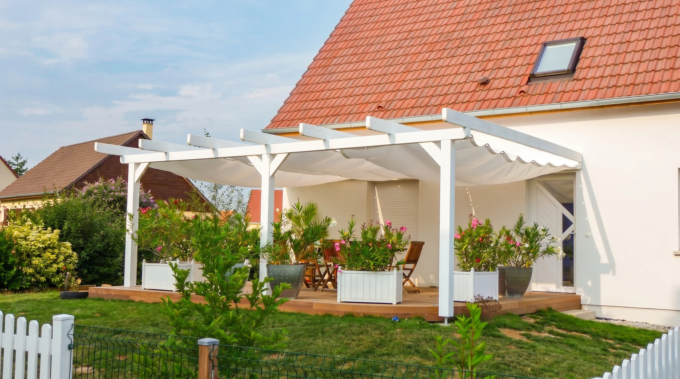 Terrasse extérieure couverte avec pergola en bois et colonnes blanches, aménagée d'un salon de jardin en résine tressée avec coussins gris sur plancher composite