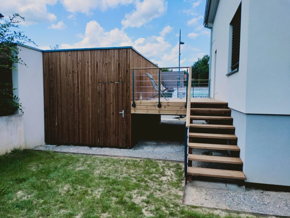 Terrasse en bois extérieure attenante à une maison moderne, entourée d'une végétation luxuriante